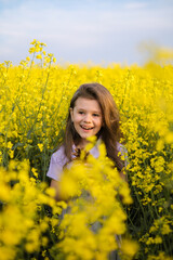 Fototapeta premium Beautiful young girl in a rapeseed field blooming in spring.