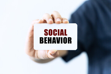 Social behavior text on blank business card being held by a woman's hand with blurred background. Business concept about social behavior.