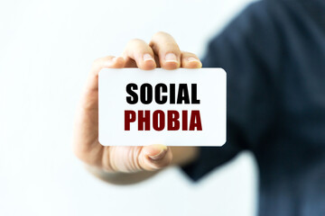 Social phobia text on blank business card being held by a woman's hand with blurred background. Business concept about social phobia.