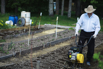 The farmer is digging a garden. A man with a harvester plows the garden. The gray-haired grandfather mows the garden.