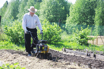 The farmer is digging a garden. A man with a harvester plows the garden. The gray-haired grandfather mows the garden.