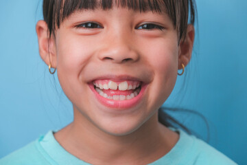 Close-up of smiling young girl revealing her beautiful white teeth on a blue background. Concept of good health in childhood. © scentrio