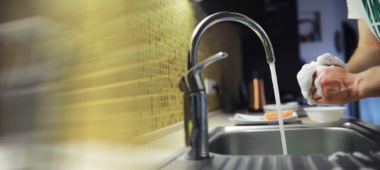 People are washing the dishes . Cleaning solution.A white bottle with dishwashing gel, sponges and rubber gloves on the background of a sink with dirty dishes.