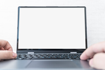 Image of Young man working in front of the laptop looking at screen with a clean white screen and blank space for text and hand typing information on keyboard in workspace.