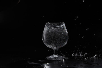 Pouring purified fresh water in glass on mirror background. Glass cup with water and bubbles on a black background