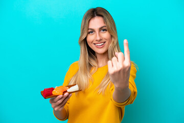 Young Uruguayan woman holding sashimi isolated on blue background doing coming gesture - obrazy, fototapety, plakaty