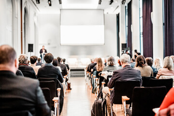 Speaker giving a talk in conference hall at business event. Rear view of unrecognizable people in audience at the conference hall. Business and entrepreneurship concept