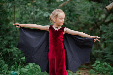 Little girl with white hair in the form of a bat in the forest. Halloween costume for a child. Waiting for a party