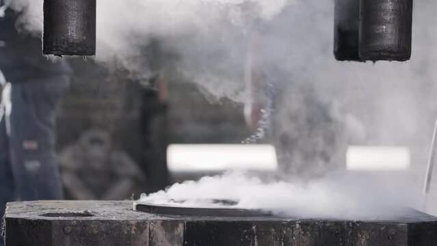 Workers preparing an industrial forging press for work with steam rising