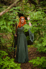 A young woman in a cloak, with a staff and a green dress in the form of a druid. Forest witch with...