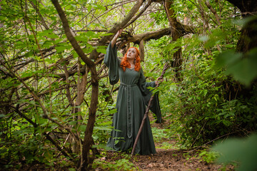 A young woman in a cloak, with a staff and a green dress in the form of a druid. Forest witch with...