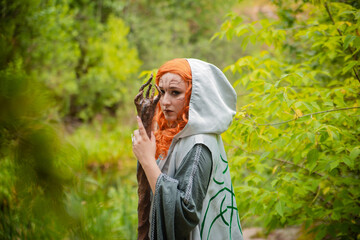 A young woman in a cloak, with a staff and a green dress in the form of a druid. Forest witch with...