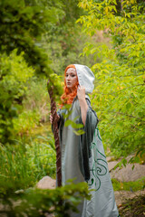 A young woman in a cloak, with a staff and a green dress in the form of a druid. Forest witch with...