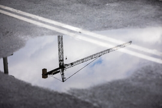 Una gr&uacute;a de construcci&oacute;n se refleja en un charco sobre el asfalto.