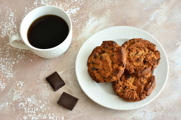 A plate of oatmeal cookies with chocolate chips next to a cup of coffee 