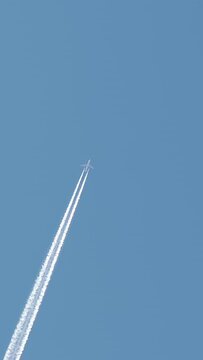 Jet aircraft plane with a bright white contrail as it flies across a blue sky. Vertical video