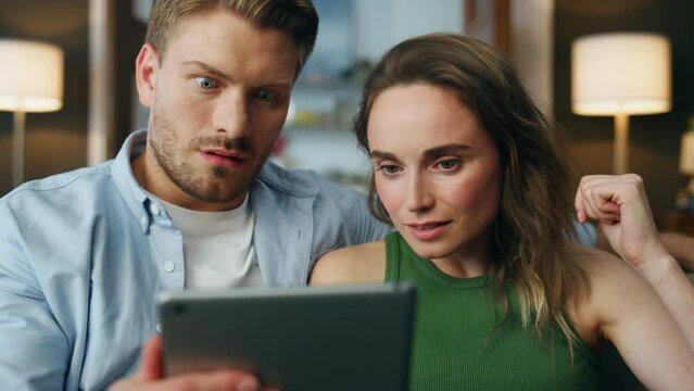Surprised pair staring tablet home zoom on. Shocked spouses faces received bills