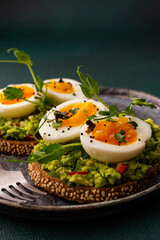 Sandwiches with rye bread and guacamole, with boiled eggs and microgreens of peas and radishes and sesame seeds, a plate with sandwiches close-up on a green background