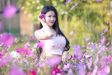 Beautiful woman happy traveler walking in the flowers garden. Young woman smile and relaxing with happy  around outdoor garden. Woman's hand touching and enjoying beauty cosmos flowers.Travel concept.