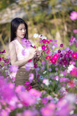 Beautiful woman happy traveler walking in the flowers garden. Young woman smile and relaxing with happy  around outdoor garden. Woman's hand touching and enjoying beauty cosmos flowers.Travel concept.