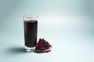 Pomegranate juice in a transparent glass and a slice of pomegranate in close-up on a blue background.