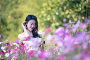 Obraz na płótnie Canvas Beautiful woman happy traveler walking in the flowers garden. Young woman smile and relaxing with happy around outdoor garden. Woman's hand touching and enjoying beauty cosmos flowers.Travel concept.