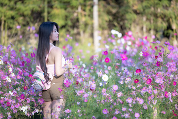 Beautiful woman happy traveler walking in the flowers garden. Young woman smile and relaxing with happy  around outdoor garden. Woman's hand touching and enjoying beauty cosmos flowers.Travel concept.