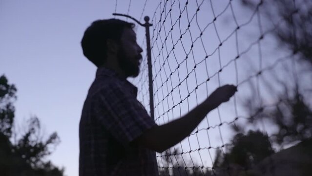 Silhouette of a man trying to find the way out behind the fencing in the evening