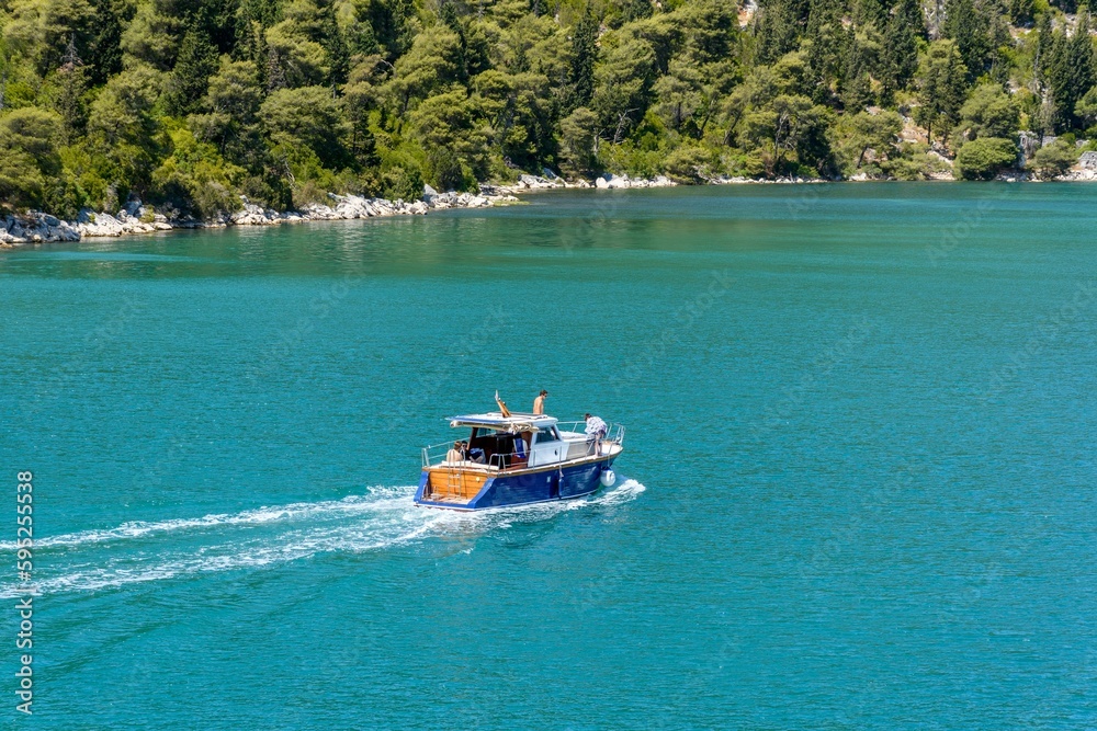 Canvas Prints Boat traversing a tranquil blue body of water, with a picturesque backdrop of trees in the distance.