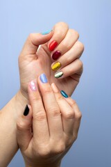 Female hands with vibrant colorful nail polish on a blue background, with an empty copy space