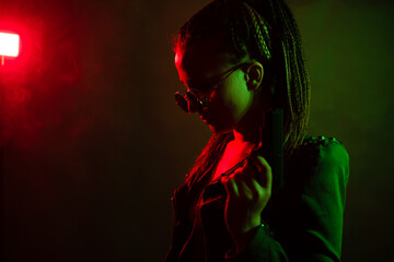 A young woman with pigtails in the dark in a club in round dark glasses holds a gun in her hands....