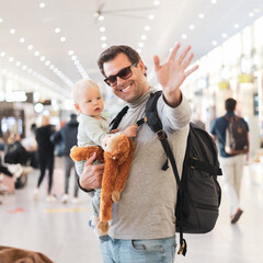 Father traveling with child, holding his infant baby boy at airport terminal waiting to board a...