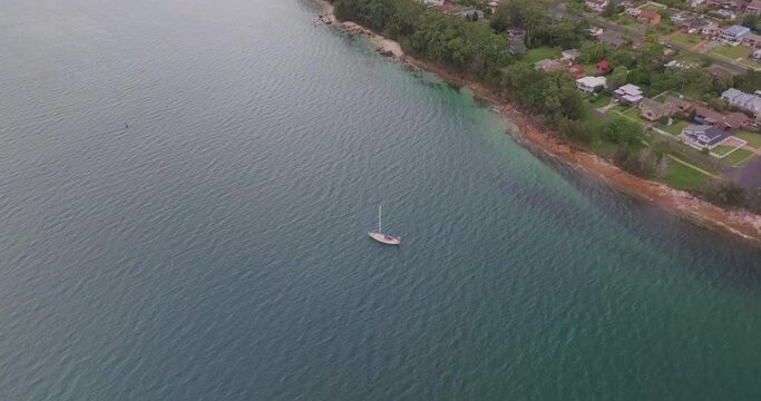 Drone view of a boat and green coastline  with trees and houses by the sea in Vincentia, Australia