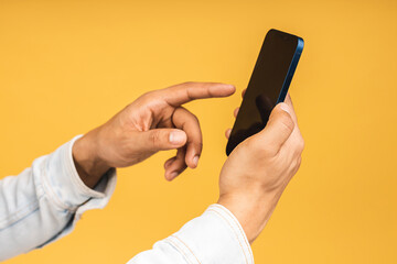 Close-up of african american young man holding phone isolated on yellow studio background with copy space aside, african guy using mobile applications, texting.