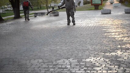 Man in protective suit spraying antiseptic solution on sidewalk in city. Persona disinfecting spray chemicals to preventing spread coronavirus. Sanitary measures in public place. Coronavirus pandemic