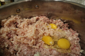 Assorted raw minced meat and eggs in a pan. Minced meat is prepared in a metal pan.