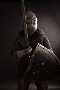 Knight with a helmet in iron armor with a shield and a sword on a black background. Medieval image. studio photo
