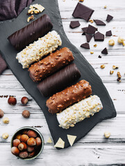 French dessert eclairs or profiteroles with different chocolate icing on a black stone plate