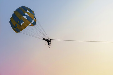 Parasailing against sundown sky. Tourist extreme entertainment on tropical seashore.