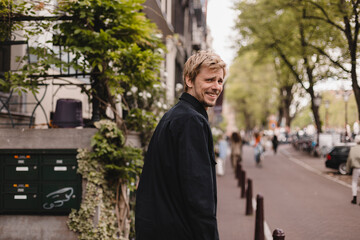 Fototapeta na wymiar Portrait of blonde man wear black shirt walk in city street. Young man turned back and looked at the camera. Lifestyle. Man look happy and smiling.