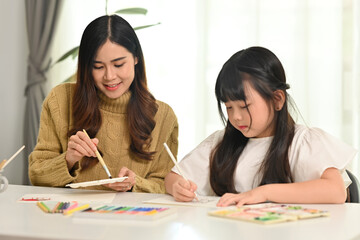 Mother and daughter drawing together in bright living room. Family home leisure concept