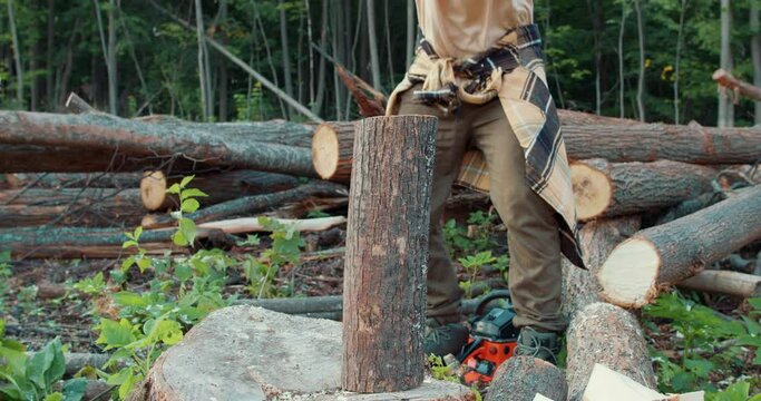 heavy axe in skilled lumberjack hands, arms chopping or cutting wood trunks. Young male in casual wear in forest at summer evening. Wood work, cutting tools, timber closeup cropped slow motion video