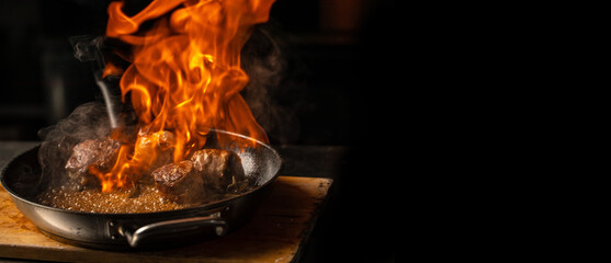 Beef steaks on the grill pan with flames on a dark background. Long banner format