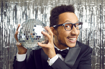 Portrait of smiling young African American man on glitter shiny background hold disco ball. Happy...