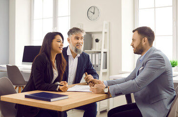 Estate agent or legal adviser talking to clients. Man and woman sitting at desk and having discussion with realtor or bank manager. Team of business partners discussing deal during meeting in office