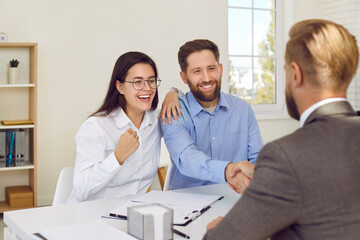 Fototapeta premium Successful deal. Husband and wife receive congratulations from bank employee on renting, buying or mortgage. Happy woman makes joyful fist while her husband shakes hands with financial advisor.