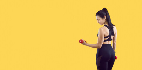 Healthy lifestyle. Smiling sporty woman with beautiful figure posing with dumbbells isolated on yellow background. Female fitness trainer in stylish and comfortable sportswear near copy space. Banner.