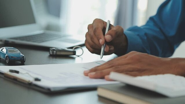 Closeup of Asian female signing car insurance document or lease paper contract or agreement. Buying or selling new or used vehicle with car keys on table.