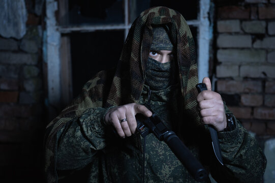 A special forces soldier in camouflage with a pistol with a silencer and a knife in his hands in an abandoned room in the twilight.