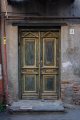 Fototapeta na wymiar Vertical photo. Facade of Georgian house. View of old vintage retro wooden closed door with scuffs and peeling green paint. City street of Tbilisi. Georgia. Concept of tourism, travel, architecture